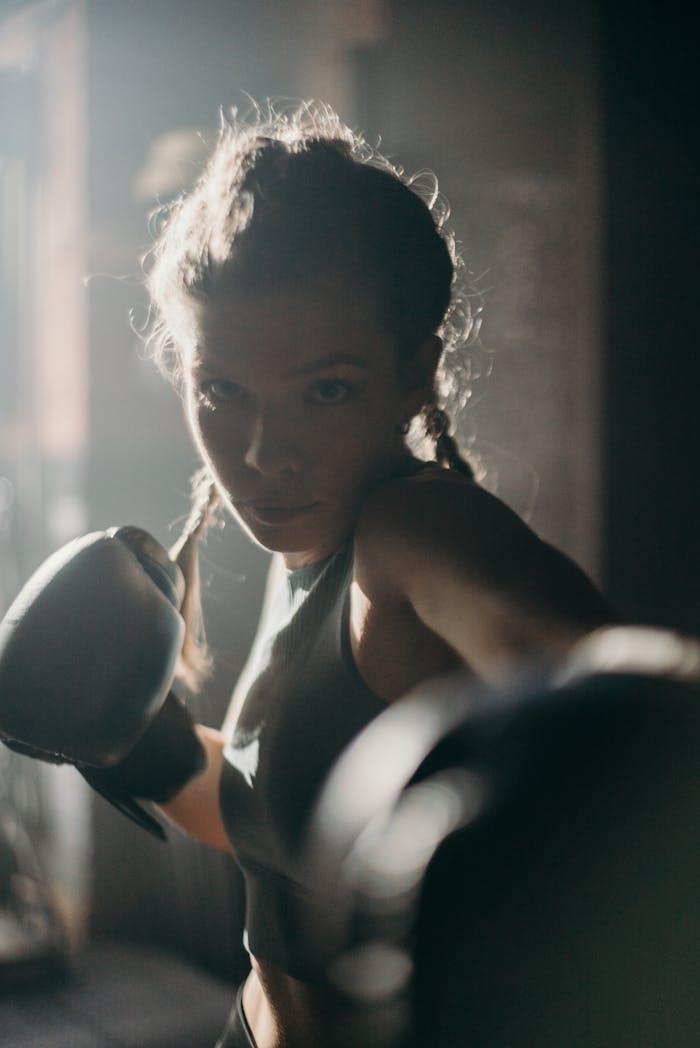 Focused female boxer in action, throwing a punch in a dimly lit gym.